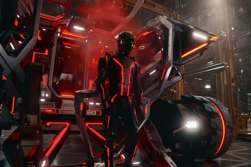 Tron Ares 2025 shows armored program warrior with red neon circuits standing beside lightcycle in Disney's sci-fi revival